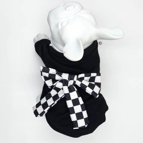 A black pet sweater displayed on a white french bulldog mannequin, featuring a large black and white checkered bow tied around the neck.