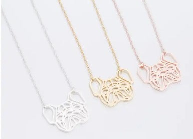 Three delicate necklace pendants with heart-shaped outlines and a central abstract cutout design, shown in silver, gold, and rose gold on a light gray background.