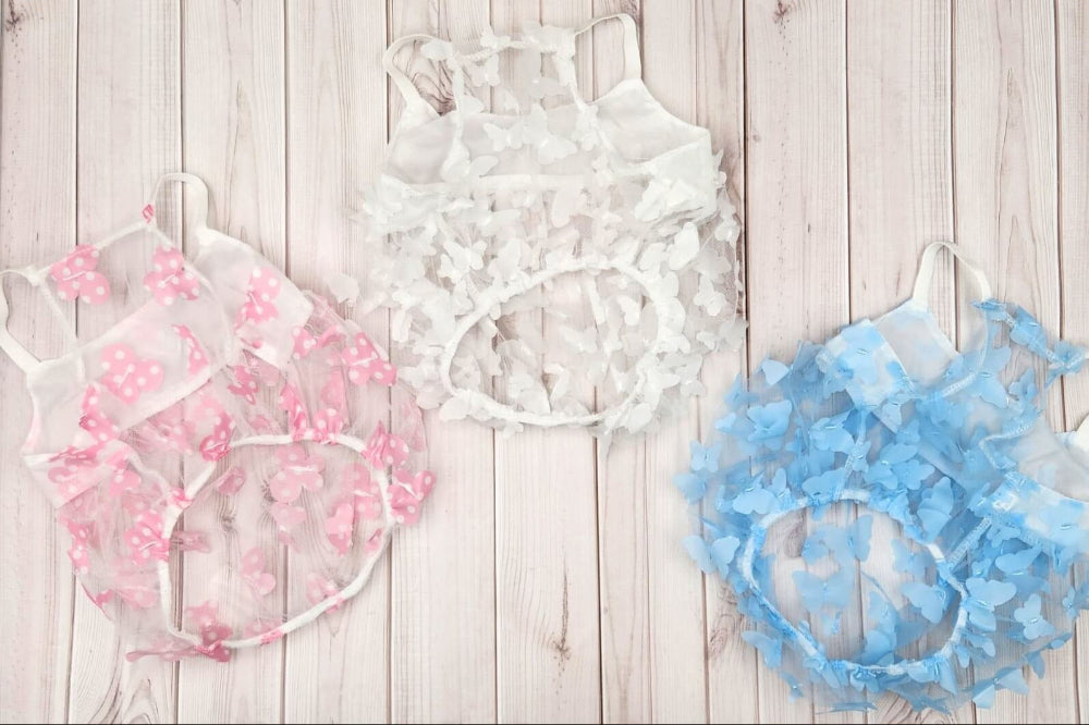 Three ruffled pet harnesses in pink, white, and blue, displayed on a light wood plank background