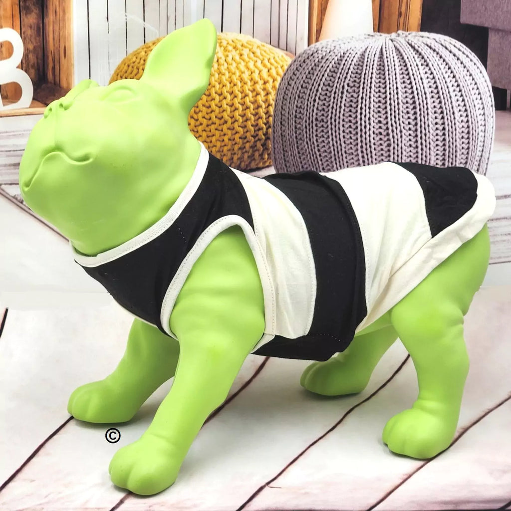 A bright green dog-shaped decorative statue wearing a black and white striped pet tank top, posed on a light wood floor with decorative pumpkins in the background.
